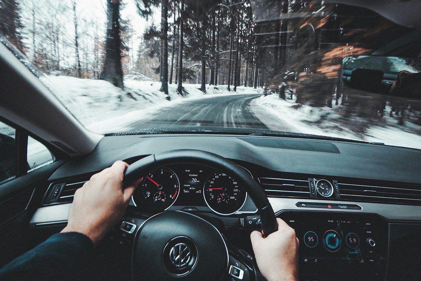 A driver's view of hands on the wheel and a snowy road ahead