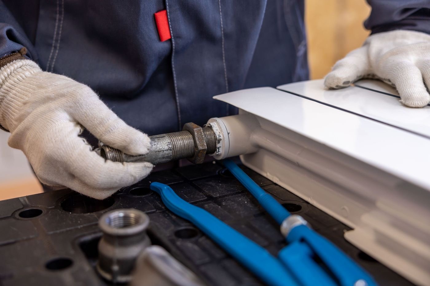 Gloved hands fitting a pipe connection with tools
