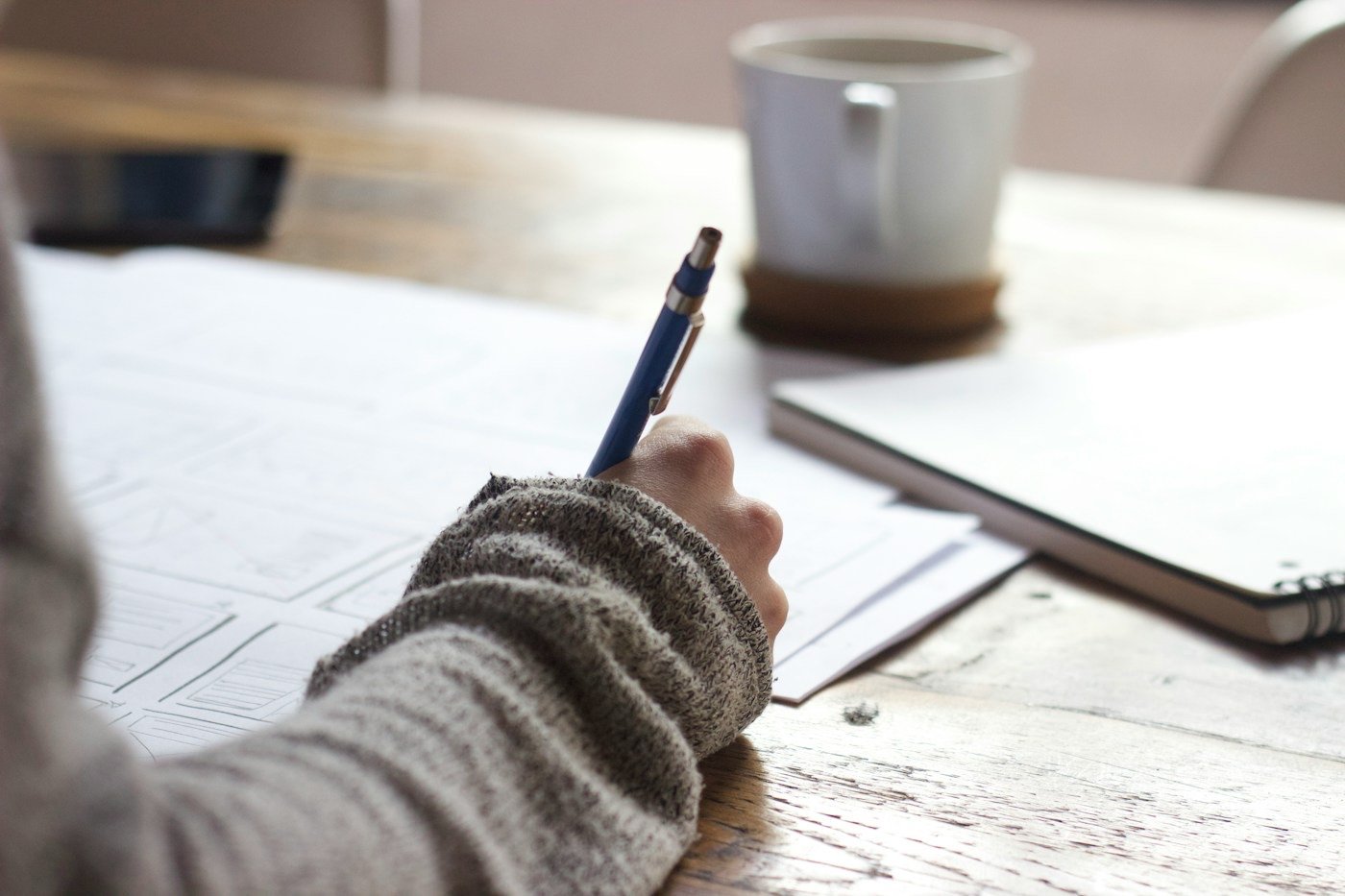 A hand writing notes on paper next to a coffee mug