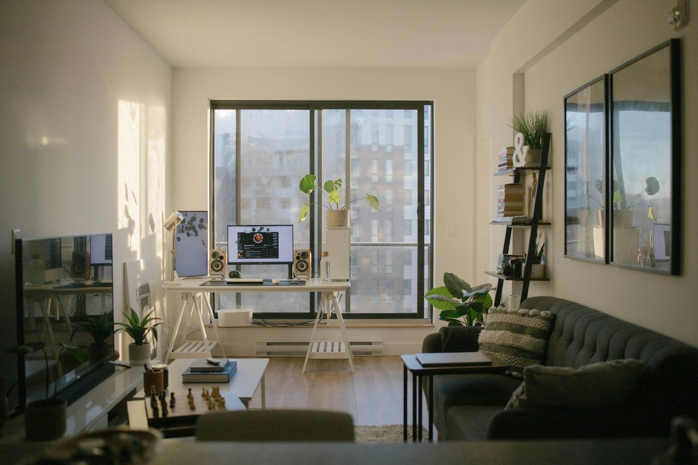 A sunlit apartment living room with a desk, sofa and plants
