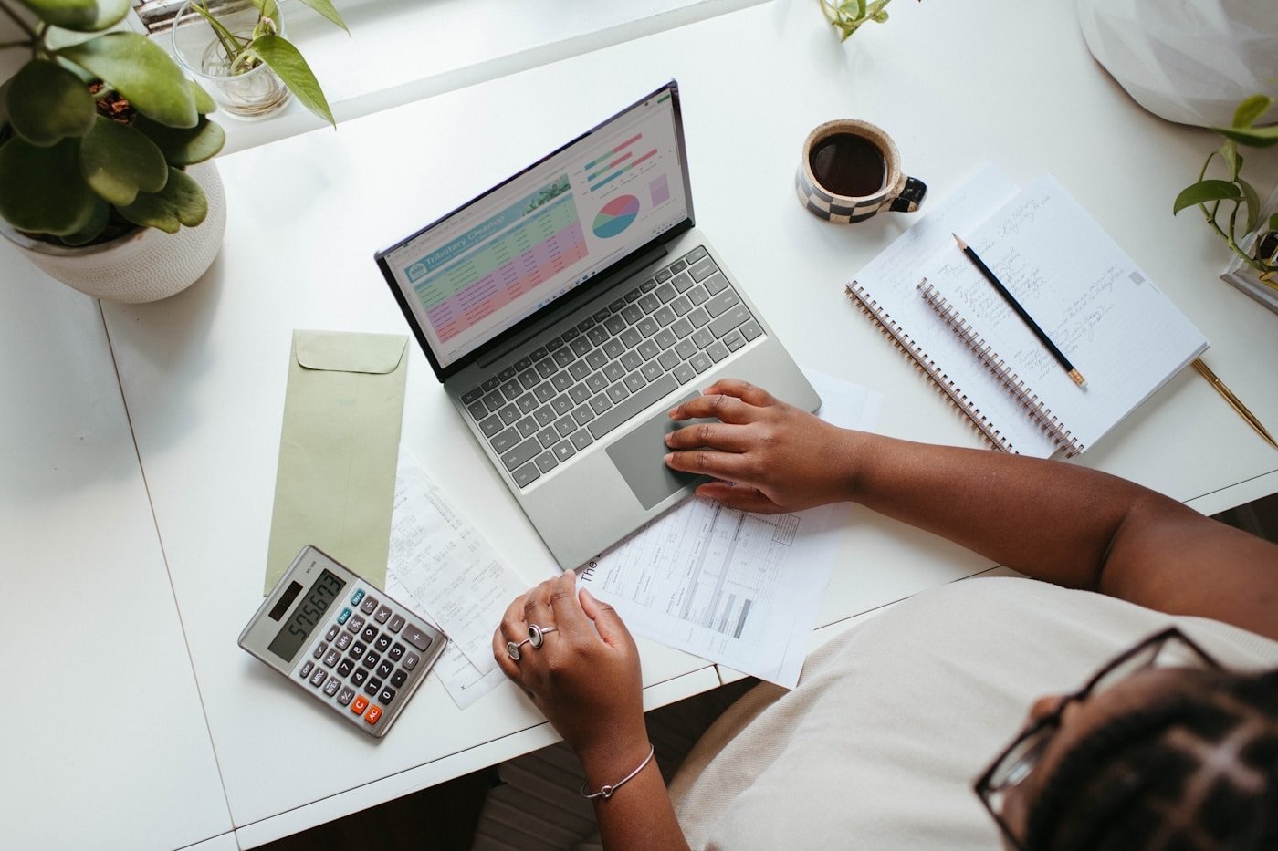 A hand at a laptop showing a budget spreadsheet, with coffee nearby