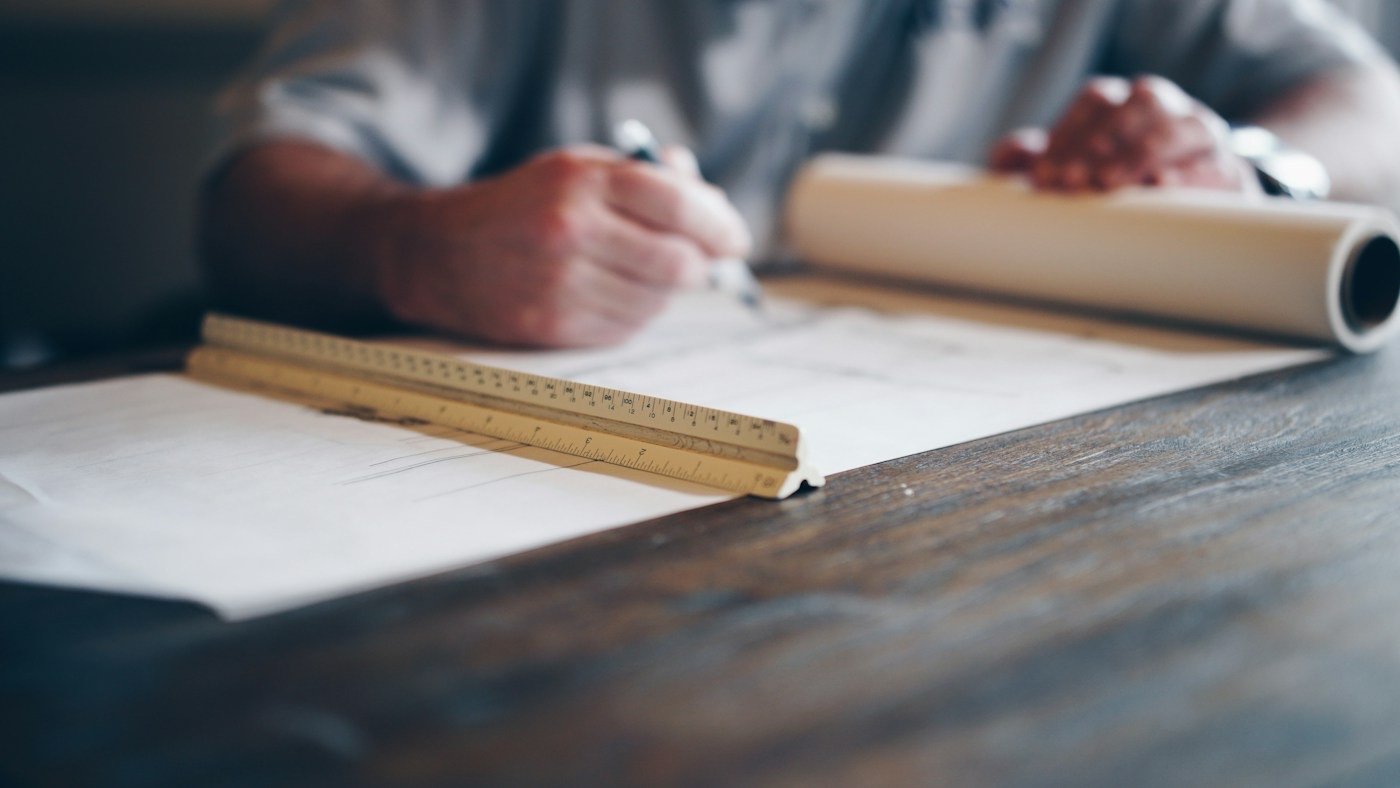 Hands drafting on a blueprint with a ruler and a rolled plan