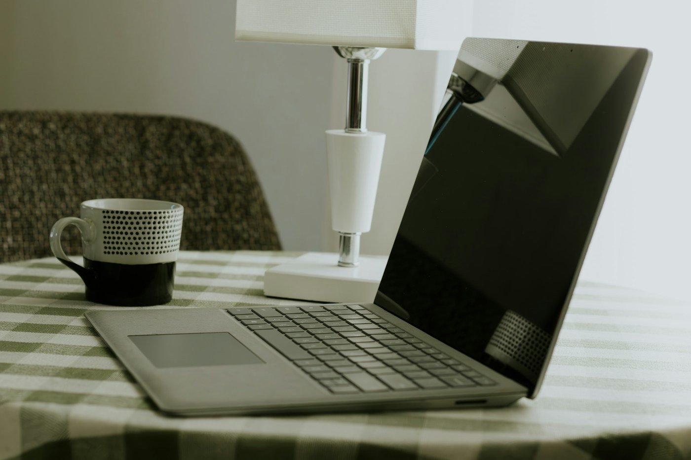 A laptop and coffee mug on a checkered tablecloth