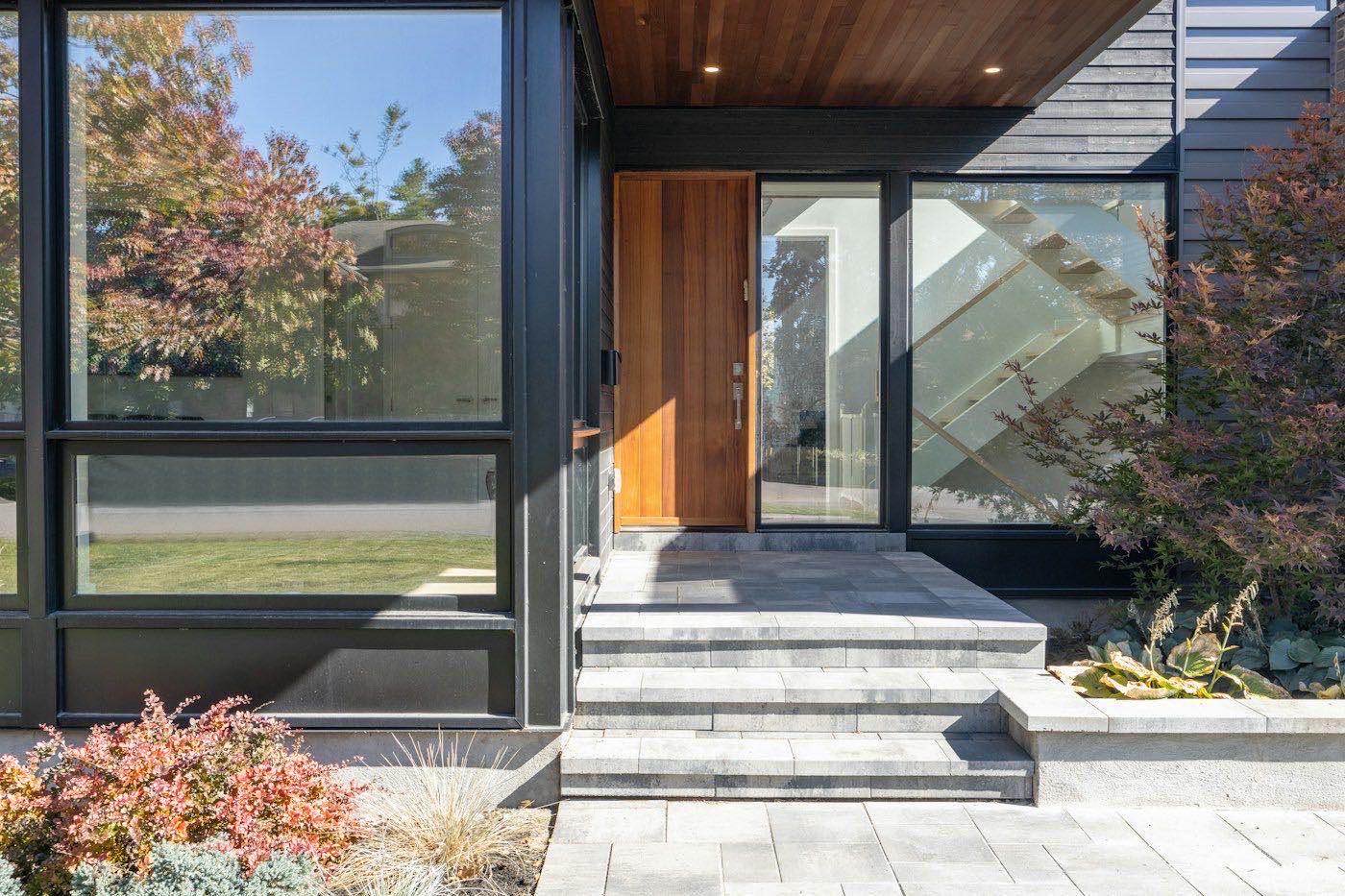 A modern wood front door flanked by tall glass windows